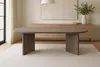 A modern oval dining table with a gray wood-look finish is shown in a well-lit dining room with a sideboard and artwork in the background. Produktbild-Vorschau