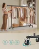 A woman is standing next to a garment rack filled with clothes. The lower half of the image shows a close-up of a wheel with locking mechanisms. Náhled obrázku produktu