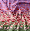 A close-up view of a fabric with a floral pattern, featuring red poppies against a purple and green background. Produktbild-Vorschau