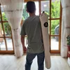 A person carrying a rolled-up mat over their shoulder, standing indoors near a large window. Náhľad obrázku produktu