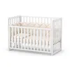 A white baby crib with beige bedding, shown from a slight angle on a white background. Anteprima dell’immagine prodotto