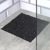 A black bath mat with a scalloped edge is placed on a gray tiled floor in a shower stall, next to white subway tiles and a glass shower door. Produktbild-Vorschau