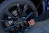A person's hand is shown adjusting a black strap on a car wheel. Anteprima dell’immagine prodotto