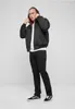 A man wearing a black hooded jacket and black jeans, posing against a white background. Produktbild-Vorschau
