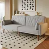 A gray sofa bed with diamond tufting is shown in a living room setting, placed on a rug with a black and white geometric pattern. The sofa has two throw pillows and is accented by a piece of abstract art on the wall. Voir les images du produit