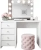 A white vanity table with drawers and a mirror with lights, next to a pink stool. Produktbild-Vorschau