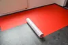 A roll of red protective fleece is partially unrolled on a gray floor next to a white radiator. Produktbild-Vorschau