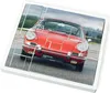 A model kit of a red Porsche 911 is shown assembled on a white base, with some pieces still separated. Náhľad obrázku produktu