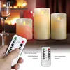 A hand holding a remote control for LED candles, with three LED candles and a wine glass in the background, set against a fireplace. Podgląd zdjęcia produktu