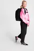 A young girl wearing a pink tie-dye sweatshirt and black pants, with a black backpack, stands against a white background. Produktbild-Vorschau