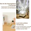 A collage of images showing a cube-shaped lamp with a textured surface, casting light patterns on a wall, and another image of the lamp on a desk with a book and a small plant. Produktbild-Vorschau