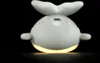 A white whale-shaped night light is shown from the back, emitting a warm yellow glow from its base. Produktbild-Vorschau