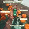 A hand holding a small bottle of hair oil, surrounded by floating orange flowers and water. Produktbild-Vorschau