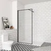 A modern bathroom with white subway tiles, a black and white patterned floor, a white toilet, and a walk-in shower with a black frame and clear glass. Produktbild-Vorschau