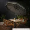 An outdoor patio scene at dusk with a table and chairs set up under a lit umbrella. Anteprima dell’immagine prodotto