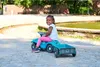 A young girl is sitting on a toy car with a trailer in a park. Produktbild-Vorschau