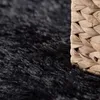 A close-up view of a black shaggy rug next to a woven basket. Produktbild-Vorschau