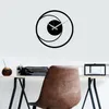 A modern black metal wall clock with a circular design is mounted on a white wall above a desk with a vintage typewriter and a brown leather chair. Anteprima dell’immagine prodotto