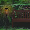 A solar-powered garden light with a flame effect is shown in a garden setting next to a wooden bench. Produktbild-Vorschau
