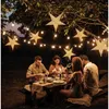 A group of people are having dinner outdoors at night, with decorative star-shaped lights hanging from trees above. Podgląd zdjęcia produktu