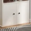 A close-up view of the lower section of a white standing bookshelf with two doors and black knobs. Produktbild-Vorschau