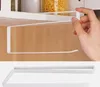A hand is shown attaching a white paper towel holder to the underside of a shelf. The bottom part of the image shows the paper towel holder on a plain background. Podgląd zdjęcia produktu
