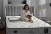 A woman is sitting on a bed reading a book, with a pillow beside her. Produktbild-Vorschau