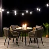 An outdoor dining set with chairs and a table is illuminated by string lights at night. Náhled obrázku produktu
