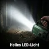 A hand holding a green emergency radio with a flashlight beam illuminating a forest path at night. Produktbild-Vorschau