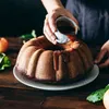 A bundt cake is being drizzled with caramel sauce by a person's hands. Anteprima dell’immagine prodotto