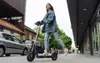 A young woman rides an electric scooter down a city street. Produktbild-Vorschau