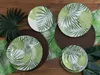 A collection of plates with a tropical leaf pattern arranged on a wooden table with decorative leaves and placemats. Náhľad obrázku produktu
