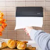 A hand pulling paper towels from a wall-mounted dispenser, with bread and flowers in the foreground. Produktbild-Vorschau