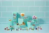 A collection of miniature toy grocery items and appliances arranged on tiered blue platforms against a light blue tiled background. Podgląd zdjęcia produktu