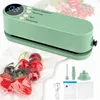 A light green vacuum sealer machine shown from a diagonal front angle, with a bundle of cherries and strawberries in a vacuum-sealed bag in front of it. Accessories for the vacuum sealer are shown in the bottom right corner. Produktbild-Vorschau