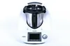 A white kitchen appliance with a stainless steel bowl and black lid, set against a white background. Produktbild-Vorschau