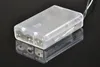 A clear plastic battery box with two battery compartments is shown on a reflective black surface. Produktbild-Vorschau