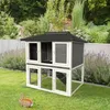A two-story rabbit hutch is set up on a green lawn in a garden, with a rabbit in the foreground. Podgląd zdjęcia produktu