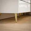 A close-up view of the bottom part of a white dresser with gold legs. Produktbild-Vorschau