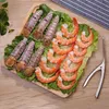 A wooden tray with a bed of lettuce holds cooked shrimp and mantis shrimp, along with a shrimp peeling tool. Produktbild-Vorschau