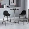 Two black bar stools are placed around a small, round black bar table with a chrome base. The scene is set in a modern interior with a gray wall and a shelf displaying books and wine bottles. Produktbild-Vorschau