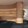 Interior view of a modern room with a curved display shelf filled with bottles and glasses, a large plant, and a glimpse of furniture in the background. Anteprima dell’immagine prodotto