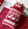 A Christmas-themed duvet cover and pillowcase set with gnomes and snowflakes, laid out on a bed with a red rug and a floor lamp. Produktbild-Vorschau