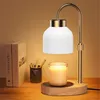 A candle warmer lamp sits on a wooden desk next to two books and a cup of pencils, with a lit candle beneath the lamp. Náhled obrázku produktu