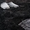 A pair of gray slippers resting on a black, high-pile rug. Produktbild-Vorschau