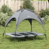 A gray dog bed with a canopy is set up on a grassy lawn in front of a wooden fence and some bushes. Anteprima dell’immagine prodotto