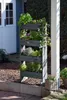 A vertical planter filled with various plants is placed outdoors next to a white building and a white pillar. Produktbild-Vorschau