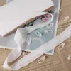 A roll of white curtain heading tape and several white curtain hooks are laid out on a surface with newspaper and magazine pages underneath. Produktbild-Vorschau