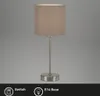 A table lamp with a taupe fabric shade and a silver metal base and stem, presented against a plain gray background. Voir les images du produit