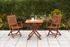 A wooden garden furniture set with two chairs and a table on a paved patio, with a hedge and flowers in the background. Produktbild-Vorschau